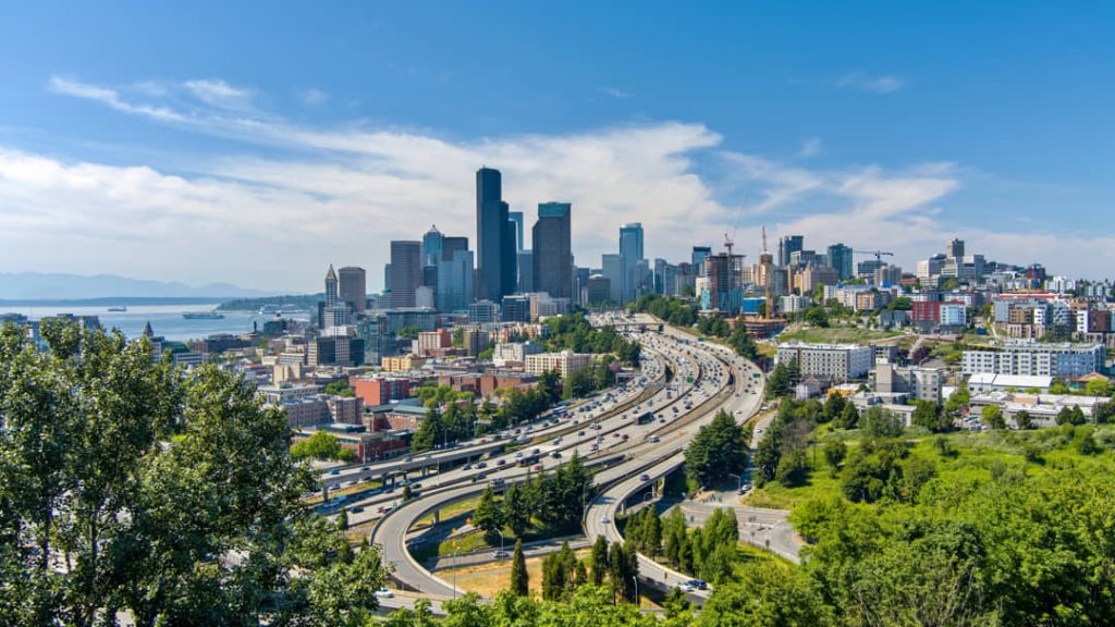 Luchtfoto van de wolkenkrabbers van Seattle met een kronkelende snelweg vol verkeer en groene heuvels op de voorgrond