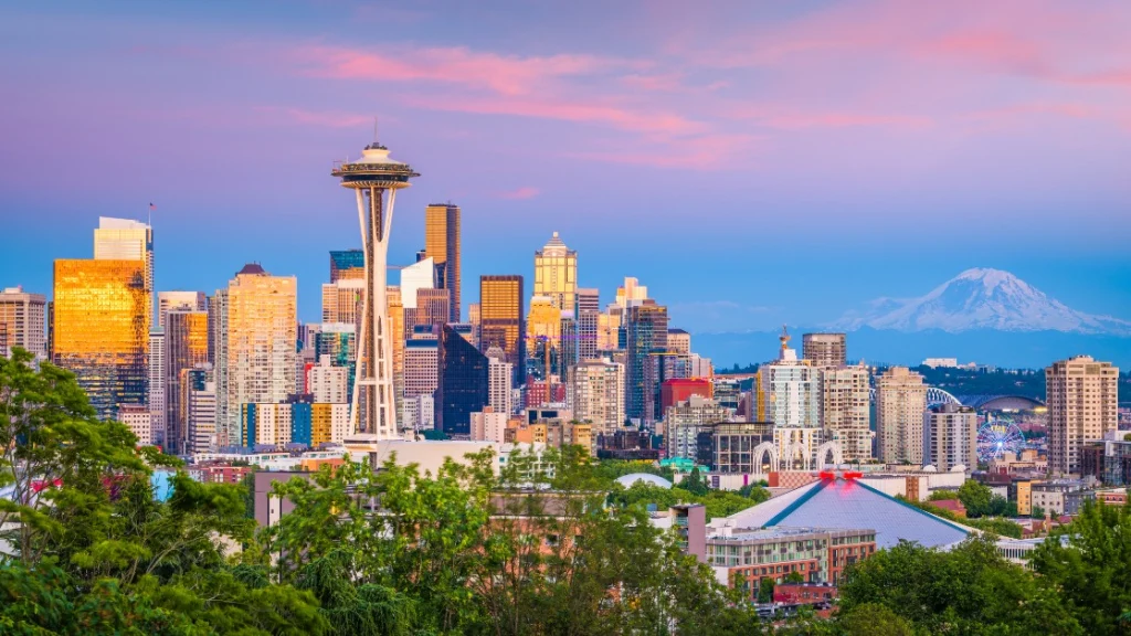 Uitzicht op de skyline van Seattle met de Space Needle en wolkenkrabbers, met de besneeuwde Mount Rainier op de achtergrond bij zonsondergang