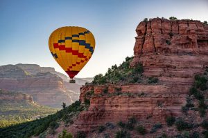 Kleurrijke heteluchtballon zweeft boven ruige rode rotsformaties en canyons bij Sedona in Arizona tijdens zonsopgang