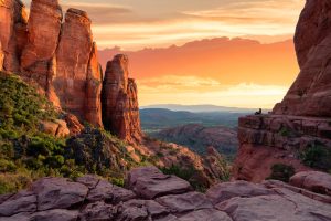 Rode rotspieken van Cathedral Rock met uitzicht over een groen dal en een oranje gloeiende avondlucht in Sedona