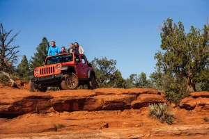 Vier mensen staan boven op een oranje jeep die op rode rotsformaties in Sedona geparkeerd staat
