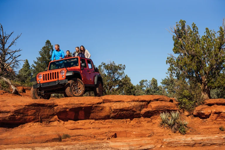 Vier mensen staan boven op een oranje jeep die op rode rotsformaties in Sedona geparkeerd staat