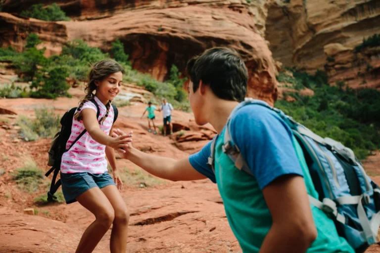 Twee kinderen met rugzakken geven elkaar een high five op een rotsachtig wandelpad tussen de rode rotsen van Sedona