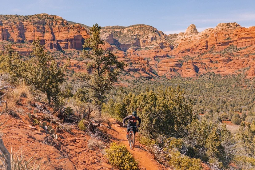 Mountainbiker rijdt over een zandpad langs indrukwekkende rode rotsformaties en groene begroeiing in Sedona
