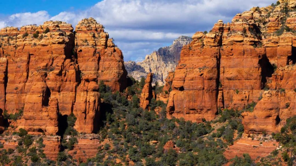 Hoge rode rotspieken en kliffen van Sedona steken boven groen struikgewas en dennen uit onder een deels bewolkte hemel