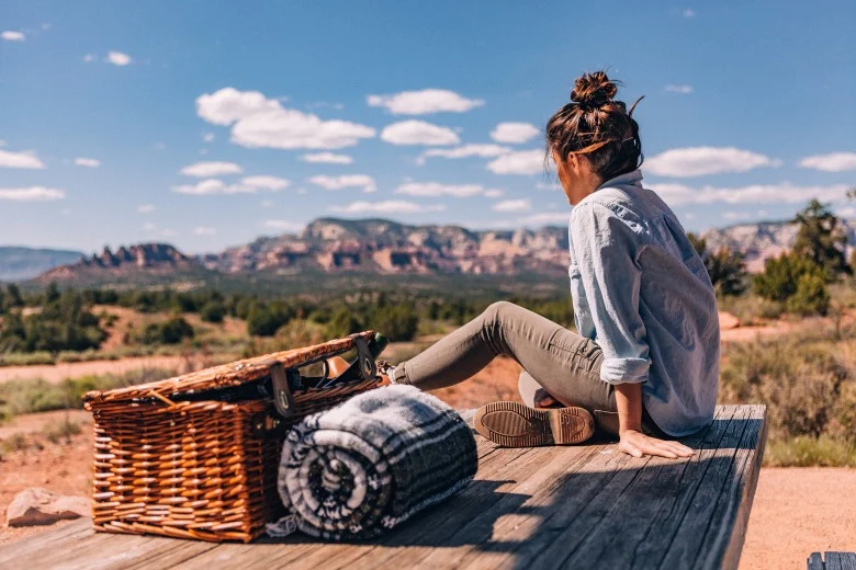 Vrouw zit op een houten platform met een picknickmand en deken en kijkt uit over het landschap van Sedona