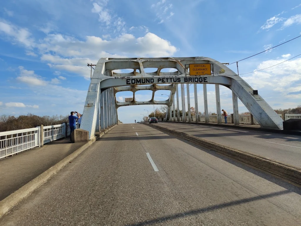 Zicht op de witte stalen boogconstructie van de Edmund Pettus Bridge in Selma met een paar wandelaars op de stoep