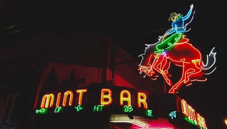 Felle neonletters met de tekst Mint Bar en een neon cowboy op een steigerend paard tegen een donkere avondlucht