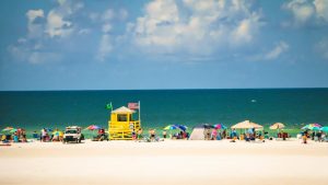 Gele reddingspost met vlaggen op een breed zandstrand vol kleurrijke strandparasols en badgasten op Siesta Key