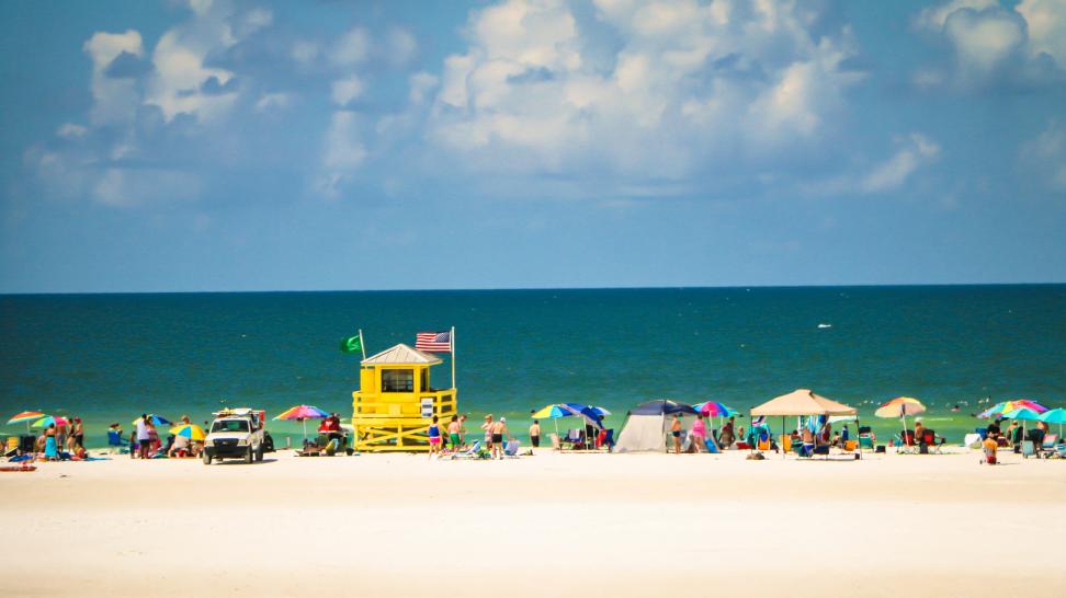 Gele reddingspost met vlaggen op een breed zandstrand vol kleurrijke strandparasols en badgasten op Siesta Key
