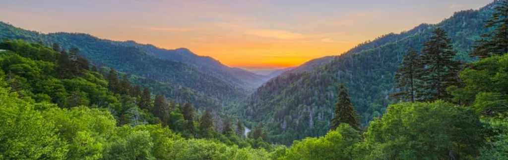 Weids uitzicht over beboste bergtoppen van de Smoky Mountains, met een gloeiende oranje lucht in de vallei