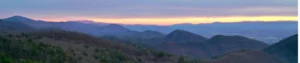 Panoramisch uitzicht over glooiende beboste bergketens in South Carolina met een zachte paars-oranje zonsondergang aan de horizon