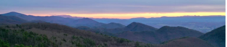 Panoramisch uitzicht over glooiende beboste bergketens in South Carolina met een zachte paars-oranje zonsondergang aan de horizon