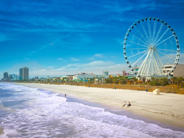 Wit zandstrand met golvende zee en op de achtergrond een groot reuzenrad en skyline aan de kust van South Carolina