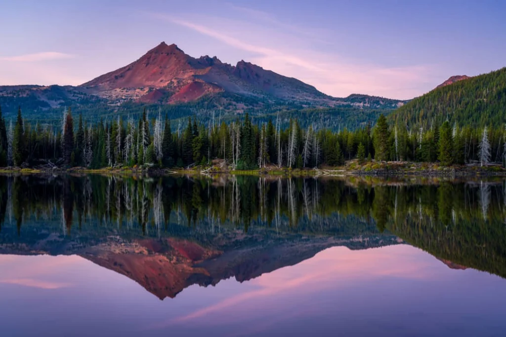 Rood gekleurde berg weerspiegelt in het rustige water van Sparks Lake omringd door dennenbos bij zonsondergang