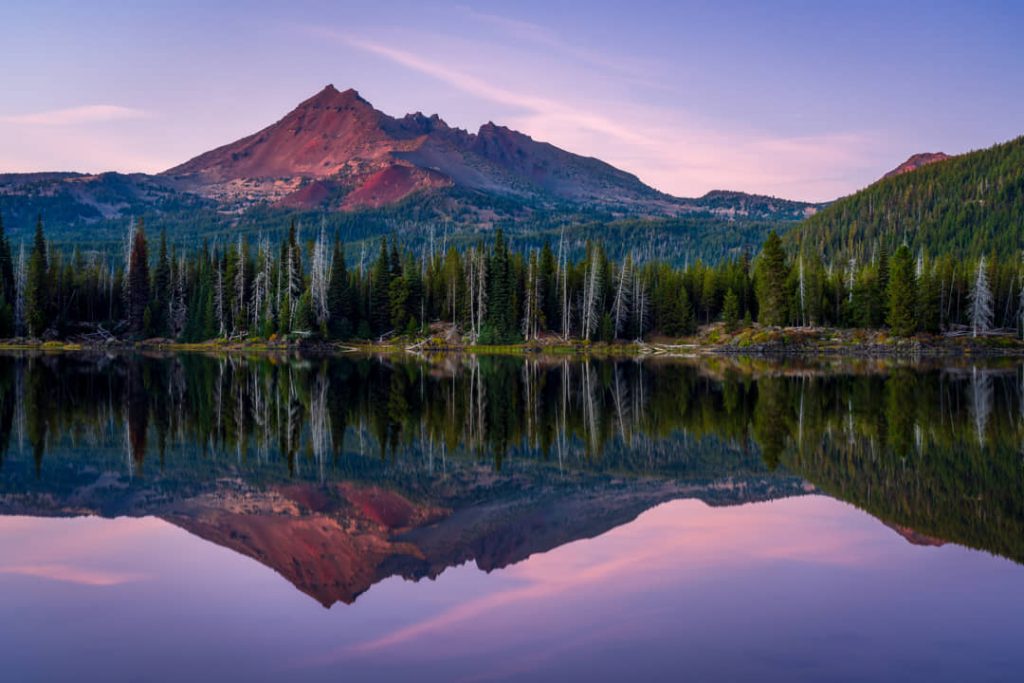 Rode bergtop weerspiegelt in het volledig kalme water van Sparks Lake omringd door bos bij het invallen van de avond