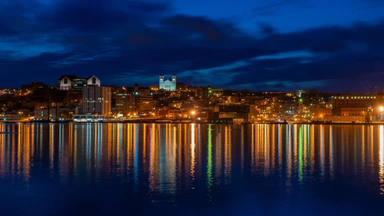Skyline van St. John's in de avondschemering met verlichte gebouwen en een kerktoren die weerspiegelen in het water