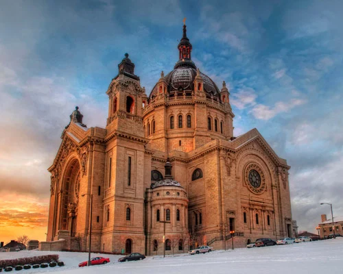 Grote stenen kathedraal met koepel en toren gezien vanaf een besneeuwd plein bij zonsondergang in St. Paul