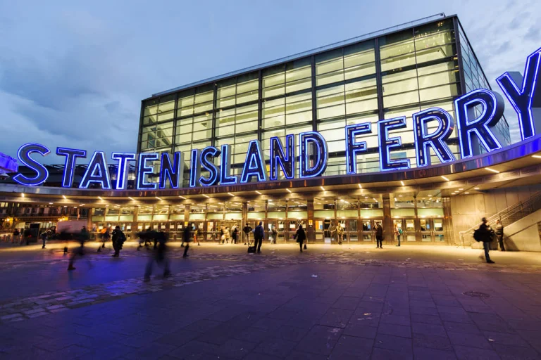 Het felblauwe neonbord Staten Island Ferry boven de ingang met mensen die in de avondschemering naar binnen lopen