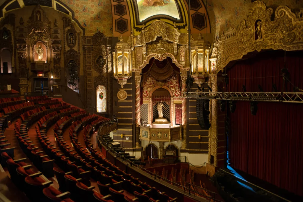 Weelderig gedecoreerd balkon met rode stoelen en een gouden proscenium boven het podium in het St. George Theatre