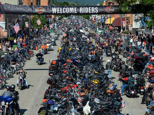 Luchtfoto toont duizenden motorfietsen geparkeerd langs de hoofdstraat onder een spandoek met de tekst Welcome Riders