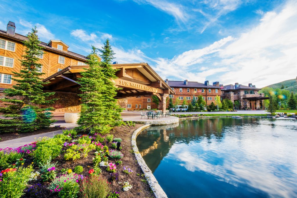 Groot houten hotelgebouw met de naam Sun Valley Lodge weerspiegeld in een vijver, met kleurrijke bloemperken op de voorgrond