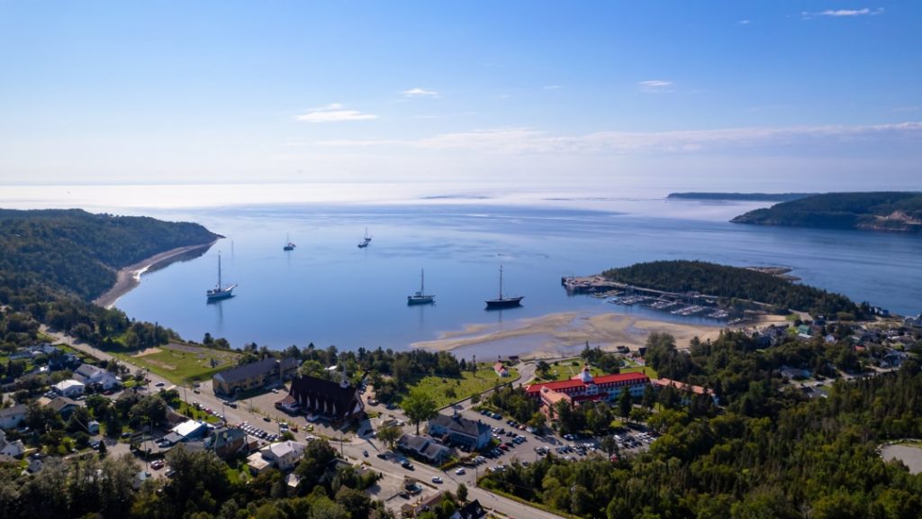 Zeilschepen liggen voor anker in de baai van Tadoussac met het rode dak van het hotel op de kust