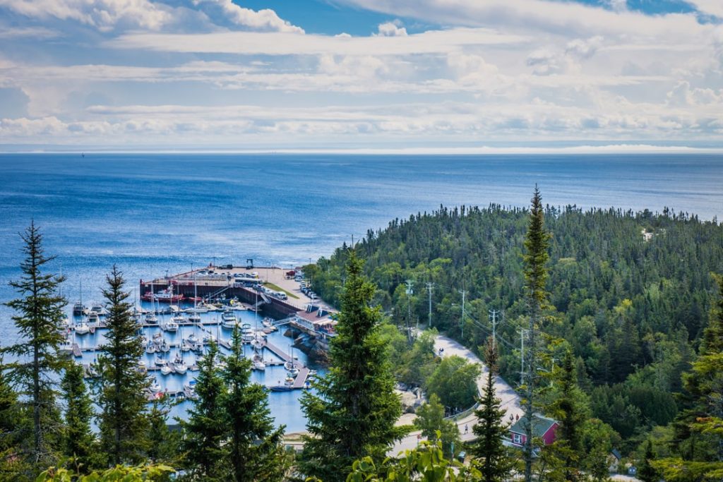 Luchtfoto van een jachthaven met bootjes aan de monding van de Saguenay, omringd door naaldbos en open zee