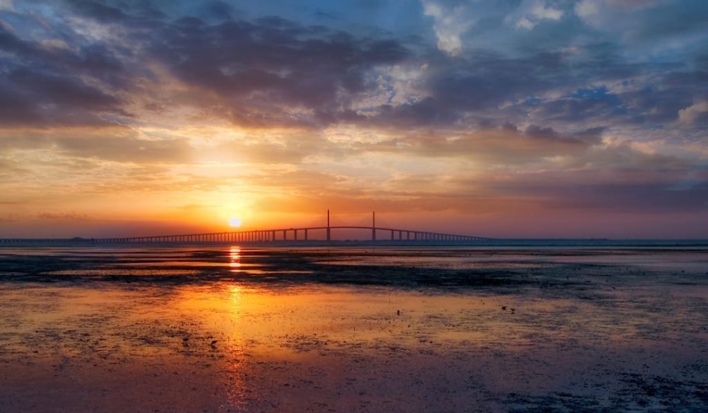 Silhouet van de kabelbrug Sunshine Skyway Bridge over kalm water tegen een oranje avondlucht