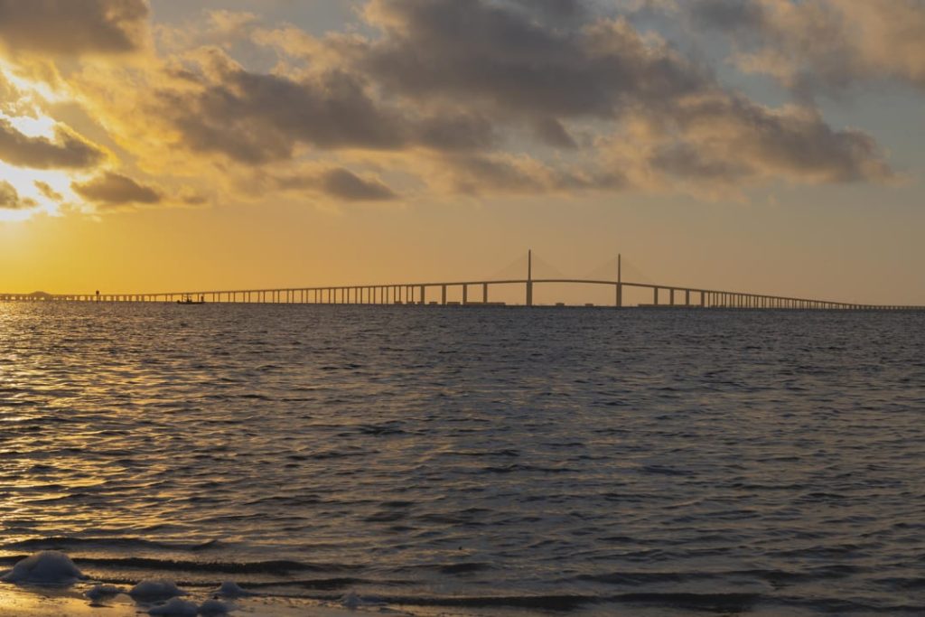 Lange kabelbrug over de baai gezien vanaf het water tegen een gouden ochtendlucht met wolken