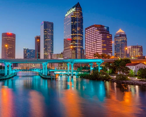 Wolkenkrabbers van Tampa met een spitse toren en een turquoise verlichte brug weerspiegeld in het water bij schemering