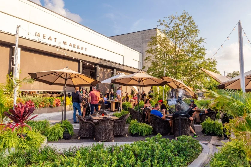 Gasten zitten onder parasols op een terras voor het restaurant Meat Market bij zonsondergang