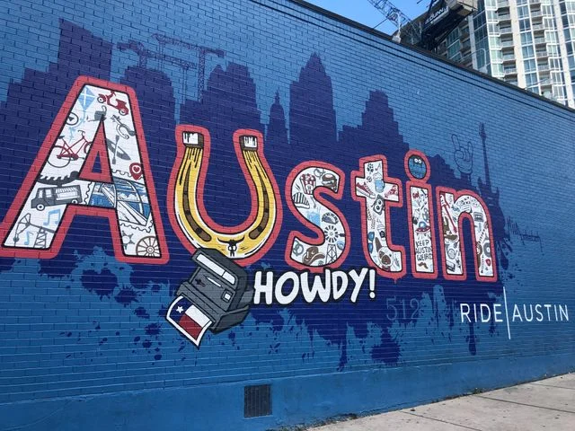 Een blauwe muur in Austin, Texas met een kleurrijke muurschildering waarop de tekst Austin Howdy staat met een hoefijzer en cowboyhoed