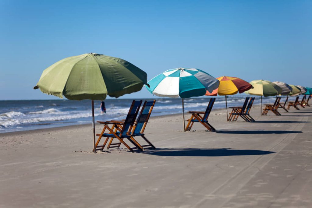 Rij kleurrijke strandparasols met ligstoelen op een leeg zandstrand aan de golfkust van Texas onder een blauwe lucht