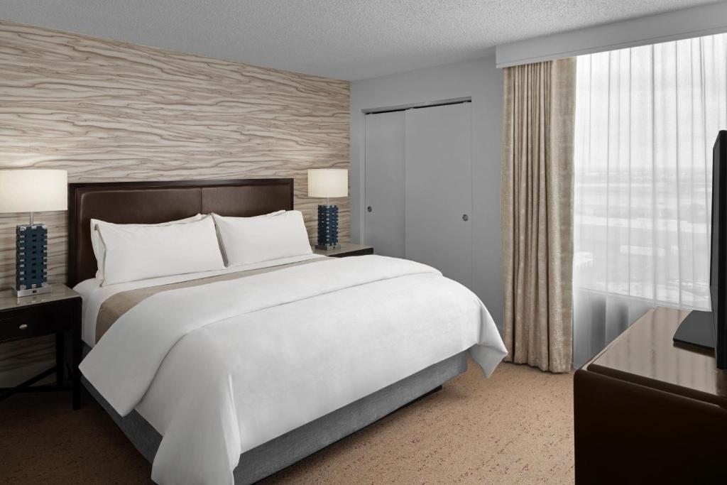Opgemaakt kingsize bed in een hotelkamer met een houten kastenwand en gordijnen voor een groot raam