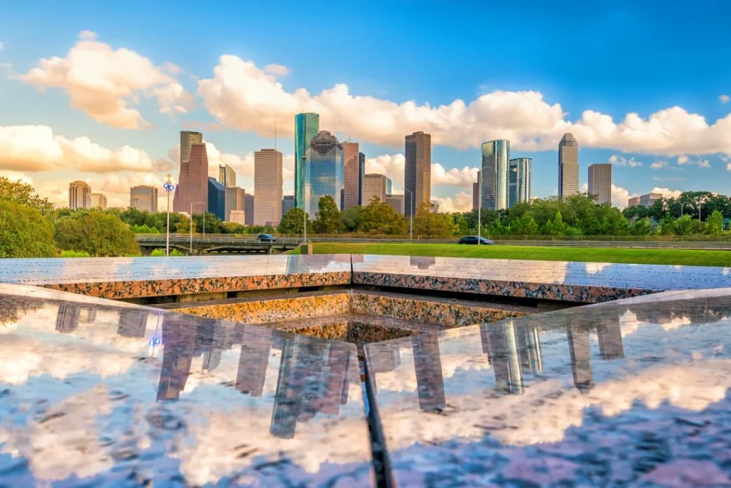 De wolkenkrabbers van Houston in Texas weerspiegelen in een rustig watervlak onder een blauwe lucht met wolken