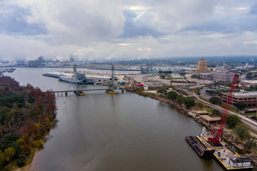 Luchtfoto van een industriele rivierhaven met een grijs marineschip, een rode kraan en fabrieken in de mist op de achtergrond