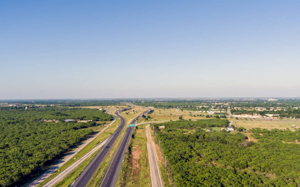 Luchtfoto van een snelweg die door een uitgestrekt, bebost heuvellandschap slingert met verspreide bebouwing in de verte in Texas