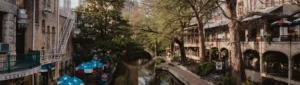 Uitzicht over de San Antonio Riverwalk in Texas met een rustig kanaal, blauw-witte parasols en historische gebouwen omringd door bomen