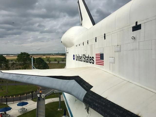 Close-up van de neus en vleugel van een witte space shuttle met Amerikaanse vlag, met bezoekers op een platform eronder in Texas