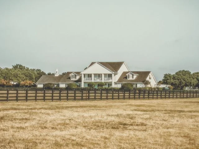 Een grote witte ranchwoning met veranda staat achter een lang houten hek in een grasveld in Texas
