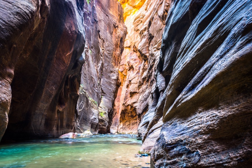 Helder turquoise rivierwater stroomt tussen hoge gestreepte rotswanden in de smalle slotcanyon van The Narrows