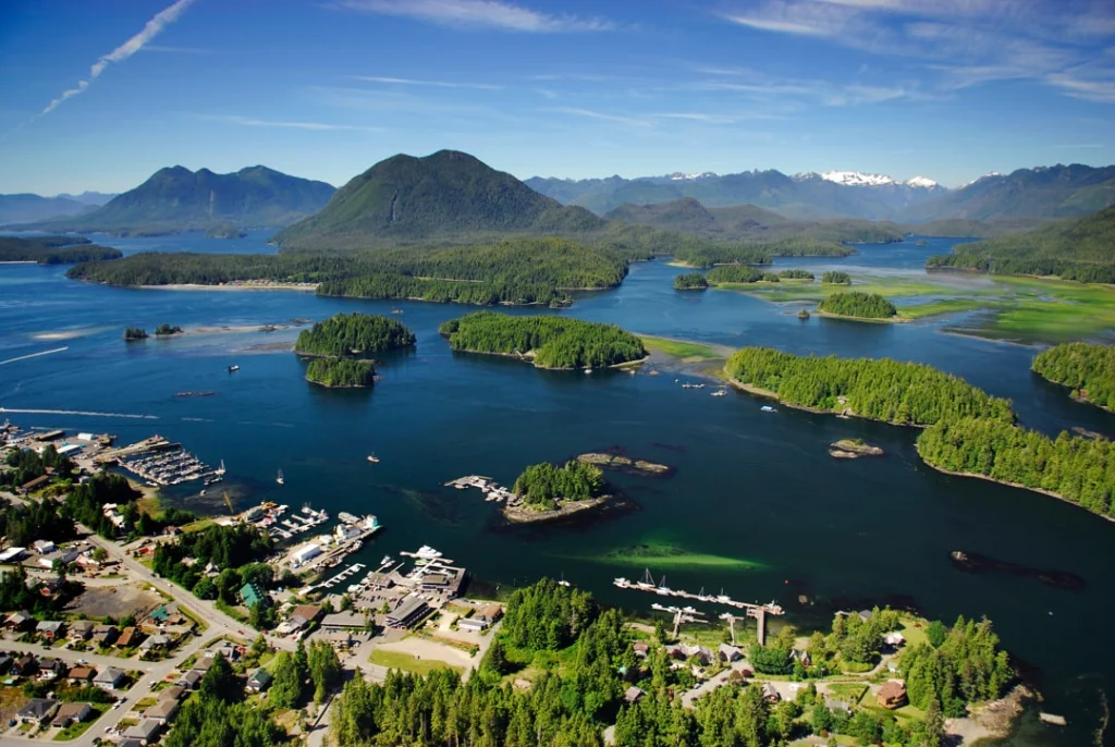 Luchtfoto van het kustplaatsje Tofino aan een baai vol beboste eilandjes, met bergen op de achtergrond in British Columbia