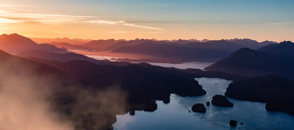Luchtfoto bij zonsondergang van de mistige kustlijn en baaien rond Tofino met glooiende bergen op de achtergrond