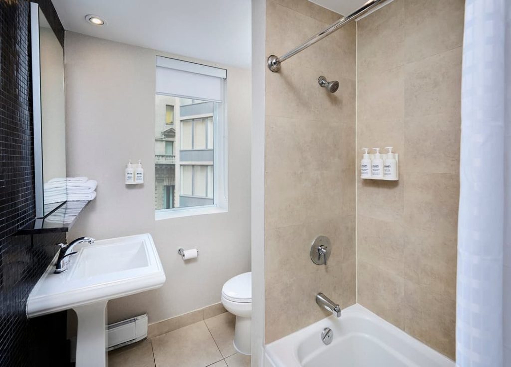 Een moderne hotelbadkamer met een ligbad, douche en wastafel in lichte kleuren bij Hotel Victoria in Toronto