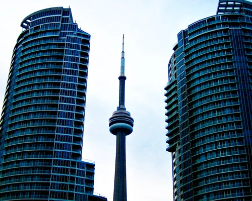 De slanke CN Tower van Toronto zichtbaar tussen twee ronde glazen appartemententorens tegen een lichte lucht