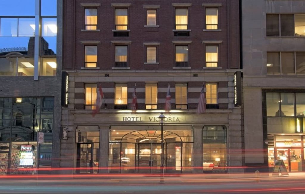 De verlichte gevel van Hotel Victoria in de avondschemering met lichtsporen van voorbijrijdend verkeer op straat
