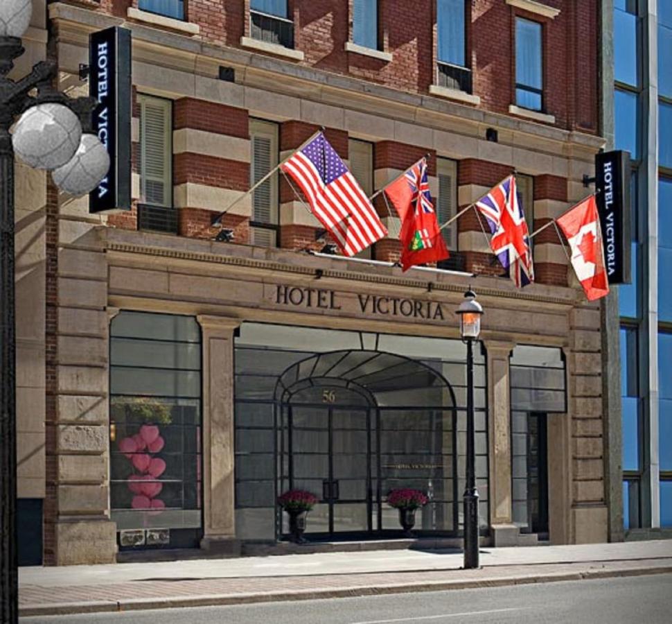 De bakstenen gevel van Hotel Victoria met vier vlaggen boven de ingang op een zonnige dag in Toronto