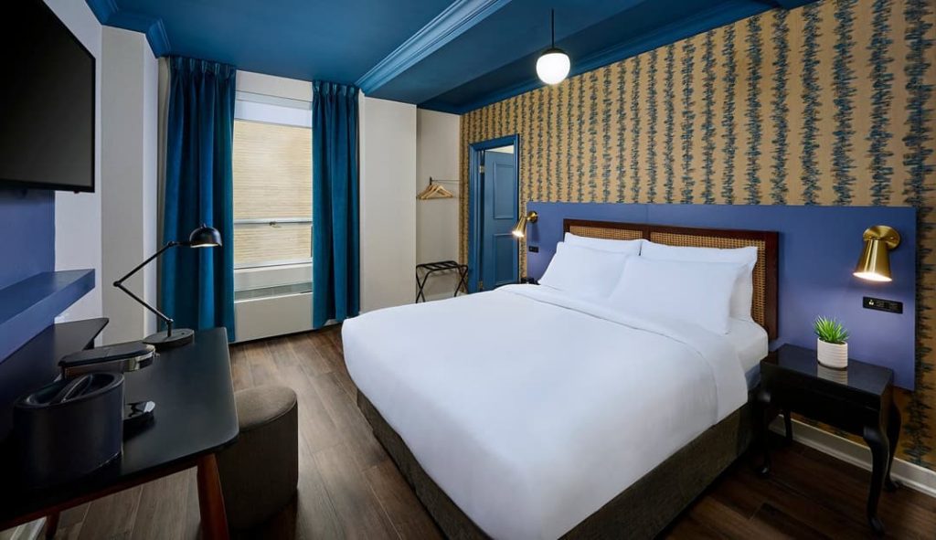 Een hotelkamer met een blauw plafond, patroonbehang en een groot wit opgemaakt bed bij Hotel Victoria in Toronto