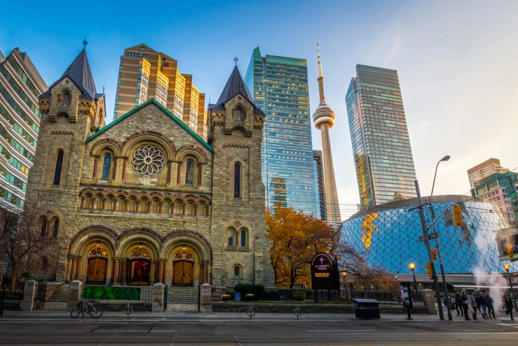 Neogotische kathedraal met torentjes in Toronto met daarachter de CN Tower en moderne wolkenkrabbers bij avondlicht